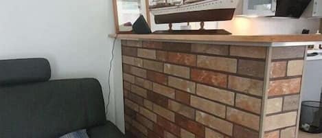 Un espace de vie comprenant un canapé, un mur décoratif en briques, une maquette de bateau et un téléviseur.