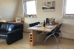 Un salon moderne avec un canapé en cuir noir, une table à manger en bois et des chaises, ainsi qu’une fenêtre donnant sur un beau paysage.