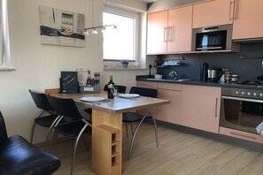 A compact kitchen with a dining area, featuring a microwave, oven, and a small table set for two. - Holiday apartment with 2 bedrooms (Cuxhaven)