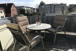 An outdoor patio with two chairs and a table, a bottle, and glasses on the table. - Holiday apartment with 2 bedrooms (Cuxhaven)