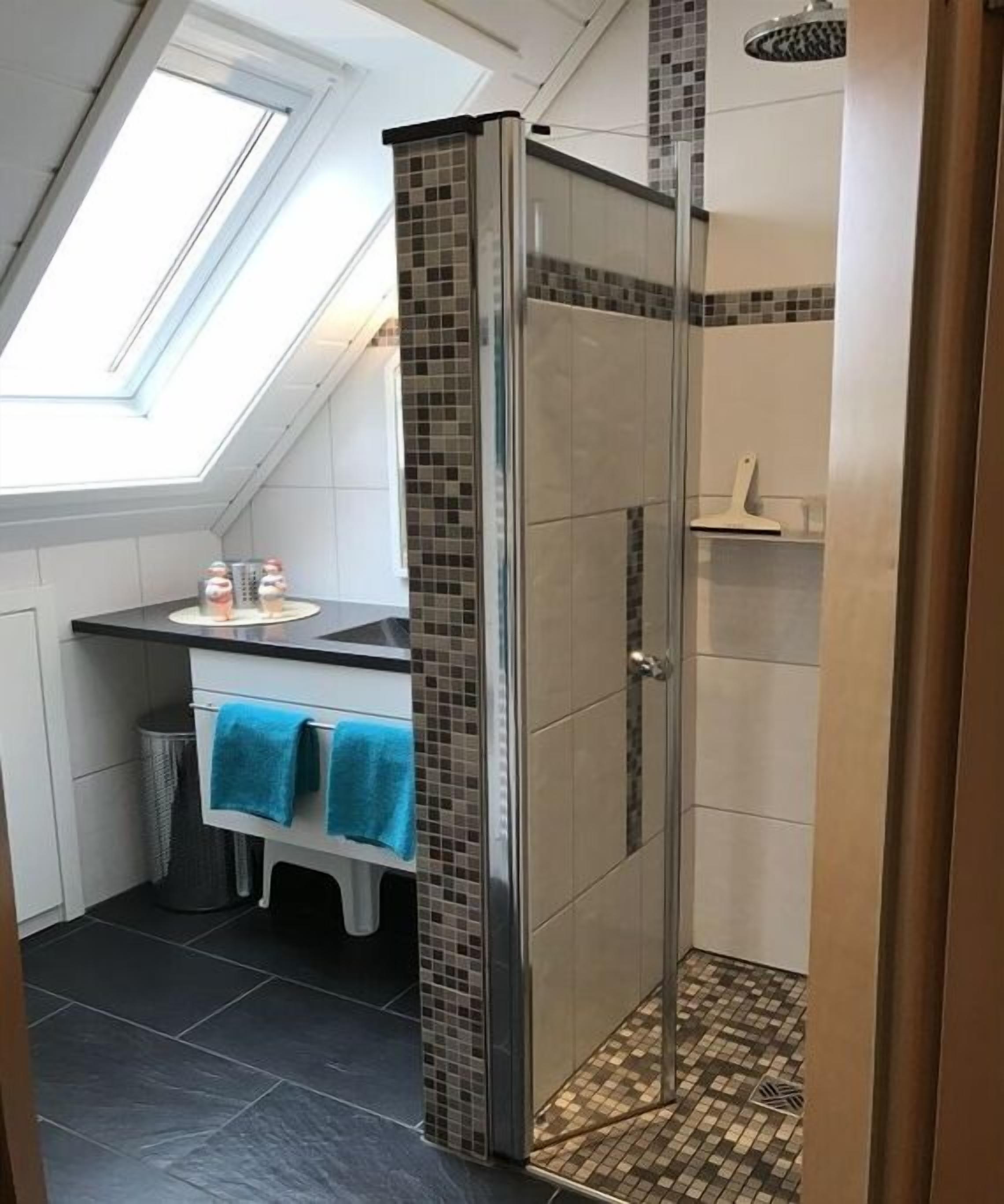 Eine Dusche mit Glastür, ein Waschbecken mit Spiegel und ein Handtuchhalter mit blauen Handtüchern.