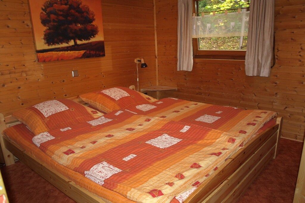 A wooden cabin bedroom with a bed, a nightstand, a lamp, and a window with curtains.