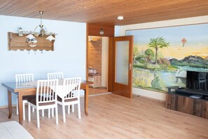 Ein Essbereich mit Holztisch und Stühlen, einer Deckenleuchte und einem wandmontierten Regal mit Dekoration.