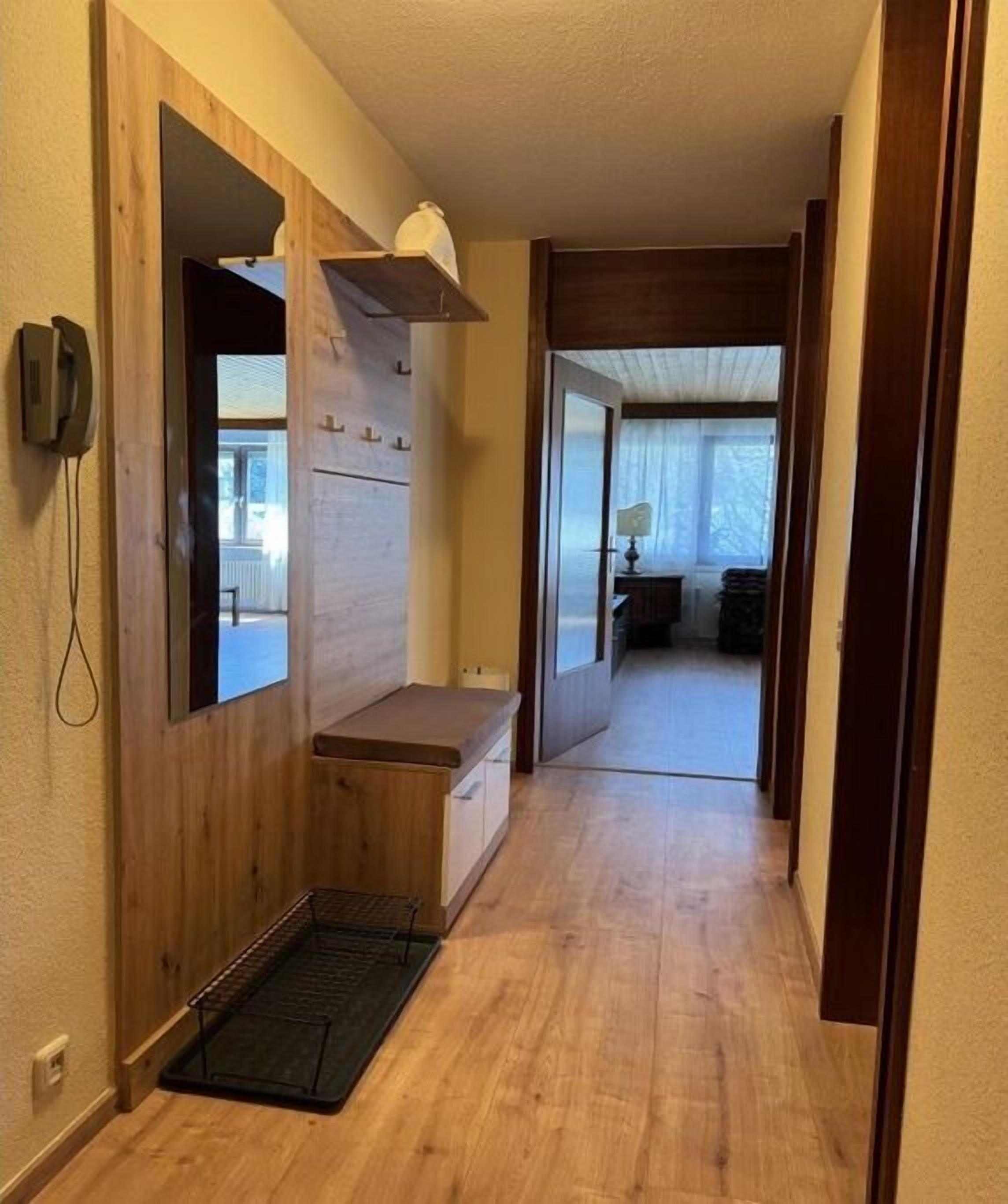 Un couloir aux murs en bois, avec un banc, un téléphone et une porte donnant sur une autre pièce.