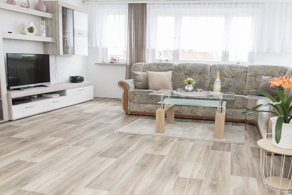 Een moderne woonkamer met een bank, een glazen salontafel, een flatscreen televisie en een witte kast.