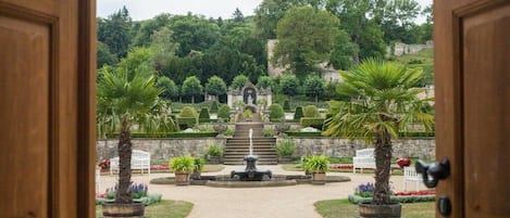 A formal garden with a central fountain, symmetrical pathways, and manicured hedges.