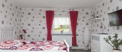 Quarto com cama, penteadeira, radiador, janela com cortinas e uma planta.