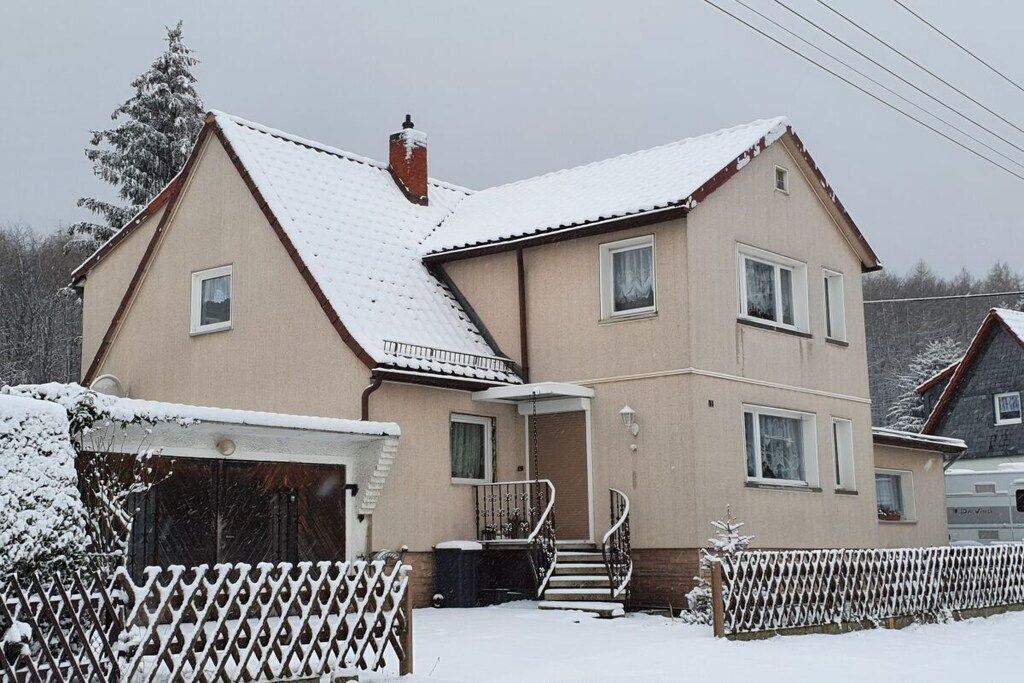 A two-story house with a snow-covered roof and a visible staircase leading to the entrance.
