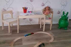 A wooden table with chairs, a doll, a green toy, and a toy train set. - Holiday home with 3 bedrooms (Blankenburg)