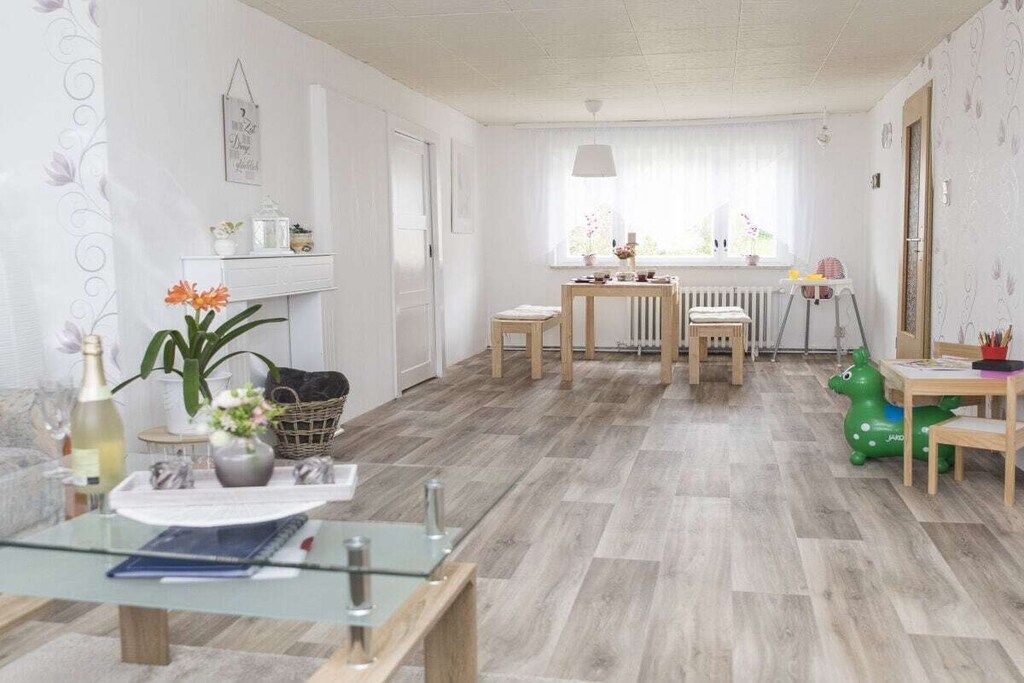 Een lichte kamer met een eettafel, stoelen, een radiator en een raam met gordijnen.