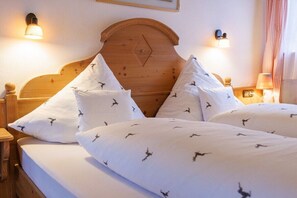 Una camera d'albergo con una testiera in legno, biancheria da letto bianca con motivi di uccelli e lampade a parete.
