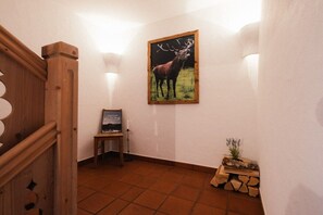 Eine Treppe mit Holzgeländern, ein gerahmtes Bild von einem Hirsch an der Wand, ein kleiner Tisch mit einem gerahmten Foto und eine Pflanze in einem Holztopf.