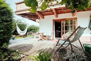 Eine Holzterrasse mit Gartenmöbeln, einer Hängematte und einem rustikalen Gebäude mit großem Fenster.