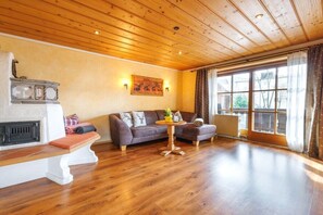 A room with a fireplace, a sofa, a coffee table, and a large window. - Holiday apartment with 2 bedrooms (Ruhpolding)