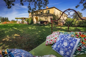 A garden with a bed, a metal bed frame, and a building in the background. - Villa Bellaria, Private Pool, Bolgheri (Bolgheri)