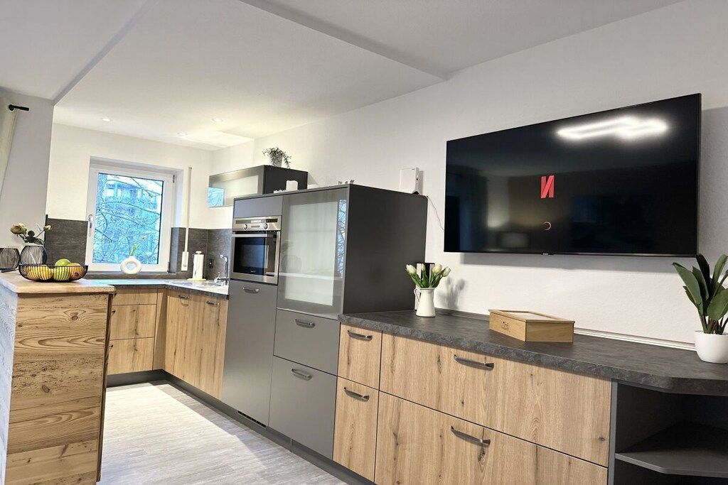 Una cocina moderna con horno empotrado, un televisor de pantalla plana grande y armarios de madera.