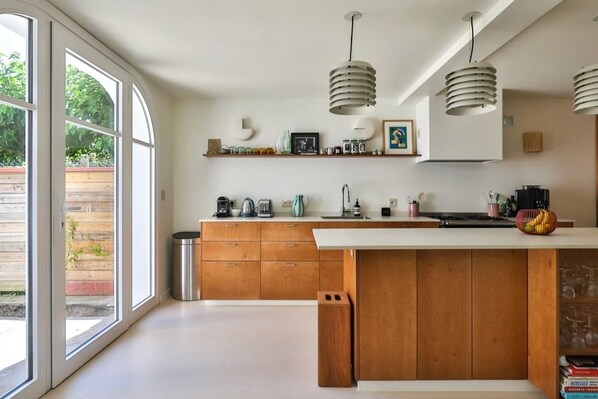 Een moderne keuken met grote ramen, houten kastjes en hanglampen.