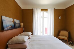 Een hotelkamer met een groot bed, een stoel, een raam met gordijnen en kunst aan de muur.