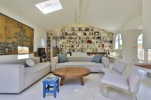 Een ruime woonkamer met een grote boekenkast, een bank, een salontafel en een schilderij aan de muur.