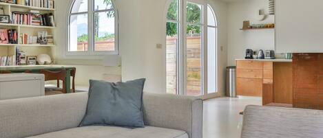 A modern living room with a sofa, a bookshelf, and a kitchen area visible through an arched window.