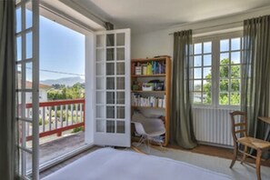 Ein Zimmer mit einer großen Schiebeglas-Tür, die auf einen Balkon führt, einem Bücherregal, einem Sessel und einem Tisch.