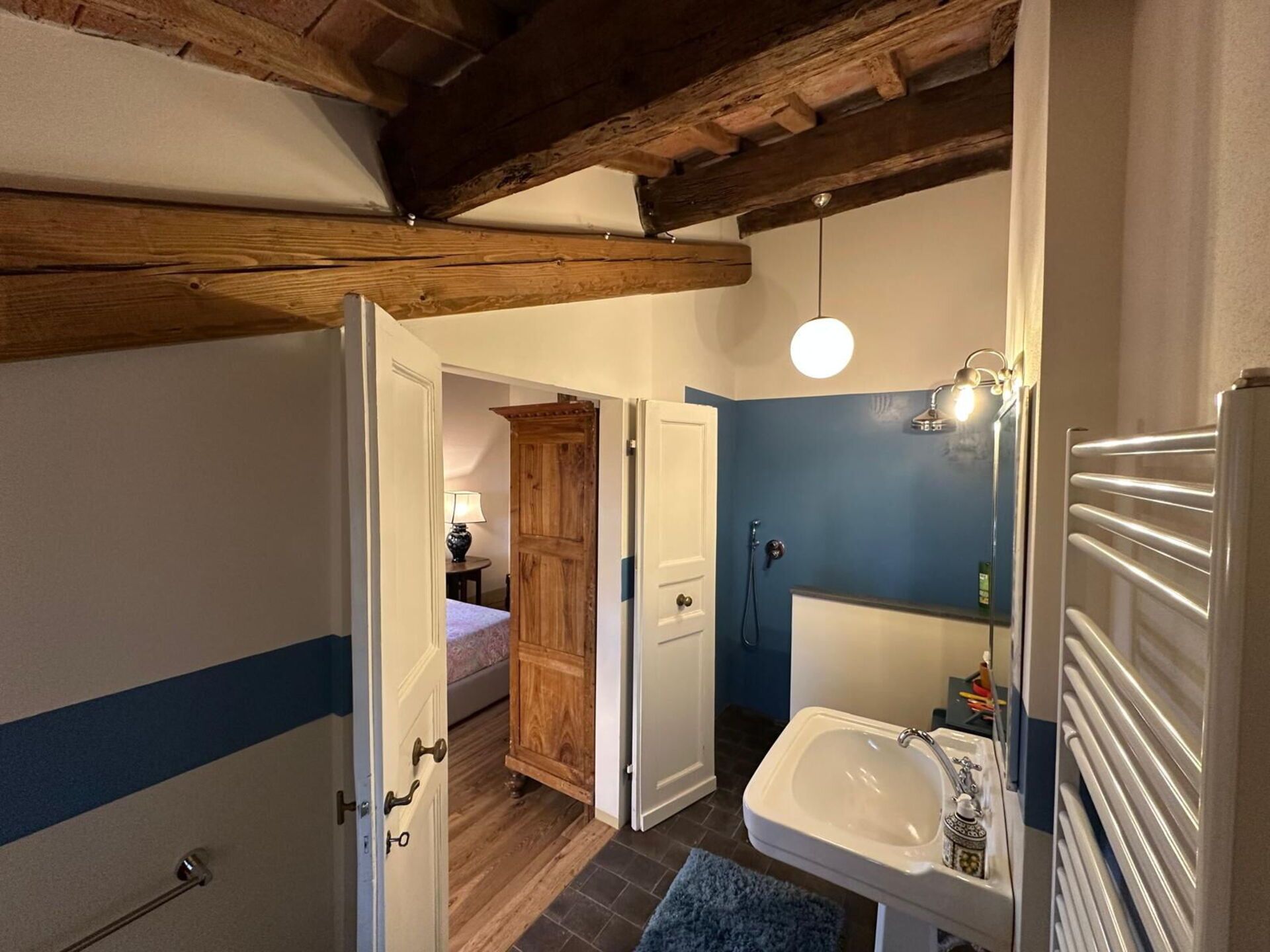 Ett hotellrum med ett träpanelat tak, ett badrum med handfat och spegel samt en säng med en blårandig vägg.