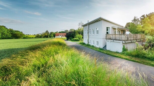 A two-story building with a balcony, surrounded by a rural landscape with a field and a road. - Beautiful living at Elm (Schöppenstedt\/Eitzum)