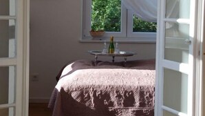 A bedroom with a bed, a window with curtains, a hanging light fixture, and a small table with a bottle. - Beautiful living at Elm (Schöppenstedt\/Eitzum)