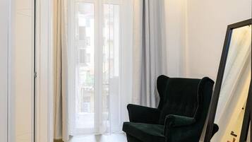 Une pièce avec un fauteuil vert, un grand miroir et une porte-fenêtre coulissante donnant sur un espace extérieur.