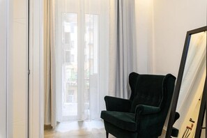 Una habitación con un sillón verde, un espejo grande y un ventanal corredero que da a un espacio exterior.