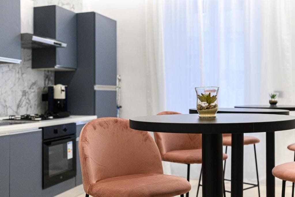 Een moderne keuken met grijze kastjes, een zwarte kookplaat en een ronde tafel met stoelen.