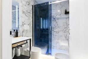 Ein modernes Badezimmer mit einer Glaskabine zur Dusche, Marmorwänden und einem weißen Waschbecken.