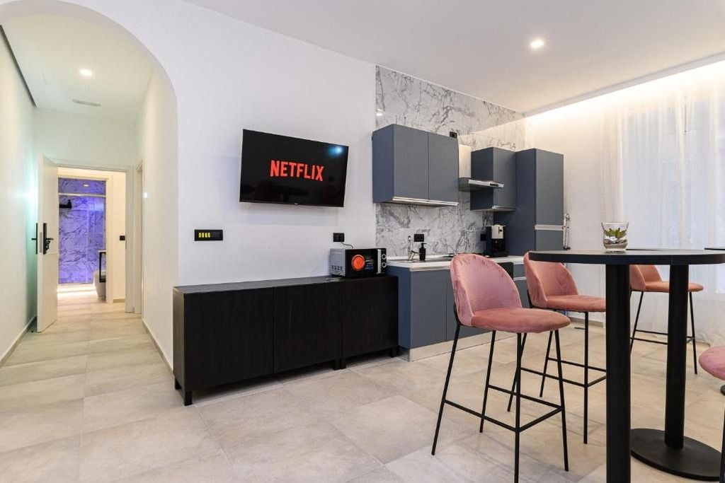 Een moderne keuken met een flatscreen televisie waarop 'NETFLIX' wordt weergegeven, een marmeren achterwand en een eethoek met barstoelen.
