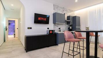 Une cuisine moderne dotée d’un téléviseur à écran plat affichant « NETFLIX », d’un pare-feu en marbre et d’un coin repas avec des tabourets de bar.