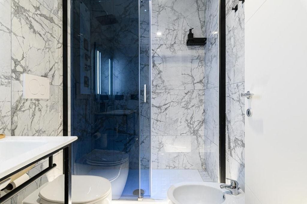 Een moderne badkamer met een douchecabine van glas, een witte wastafel en een toilet.