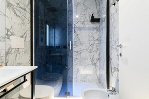 Un baño moderno con ducha envuelta en vidrio, un lavamanos blanco y un inodoro.