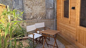 Ein Holz-Sitzbereich im Freien mit einer Steinwand im Hintergrund, einer Holztür und einem Fenster.