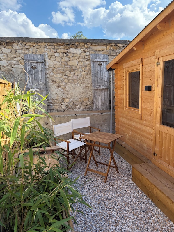 A wooden outdoor seating area with a stone wall backdrop, a wooden door, and a window.