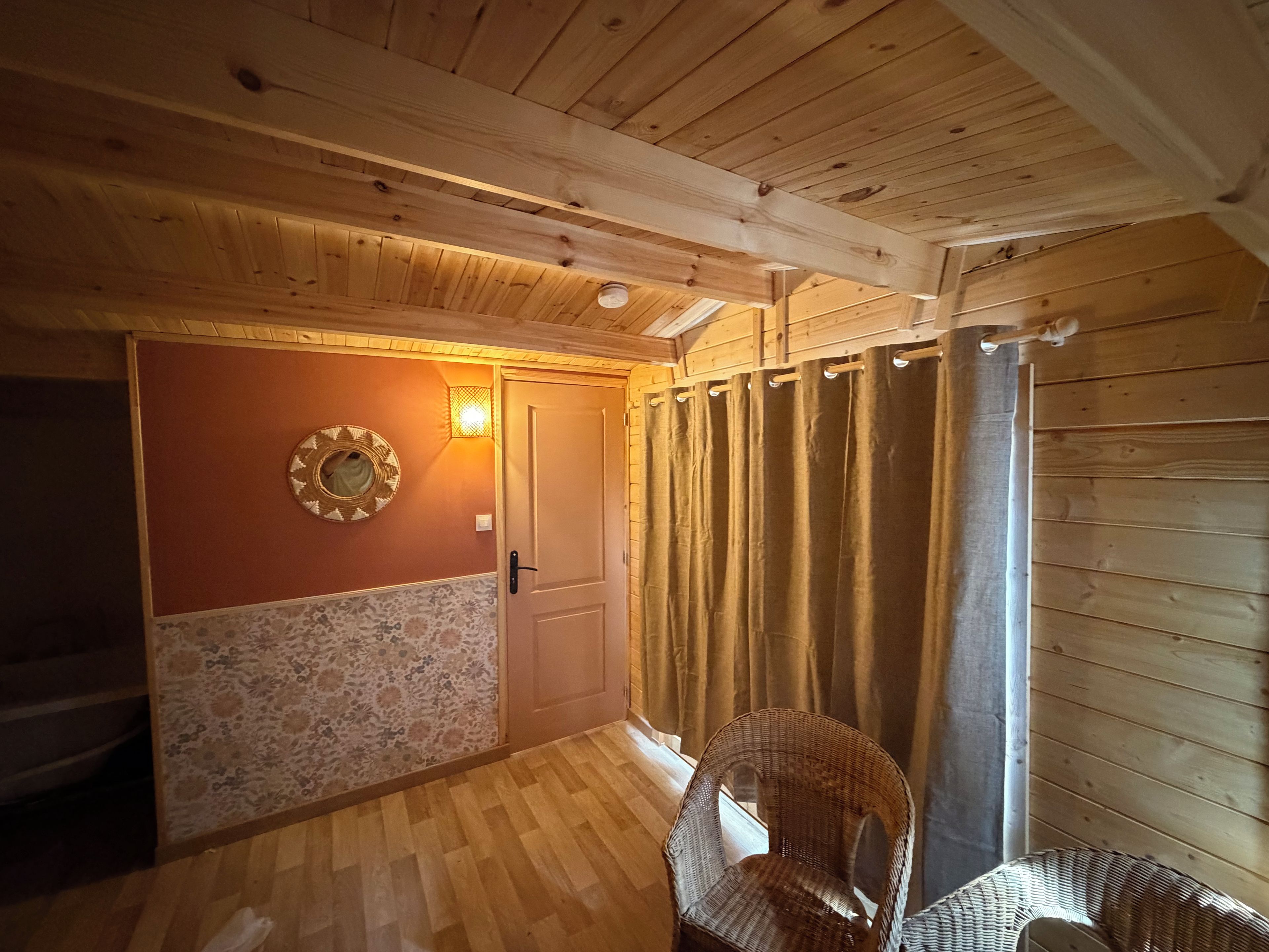 Ein Holzinnenraum mit einer Tür, einem Korbstuhl und einer Wand mit Muster.