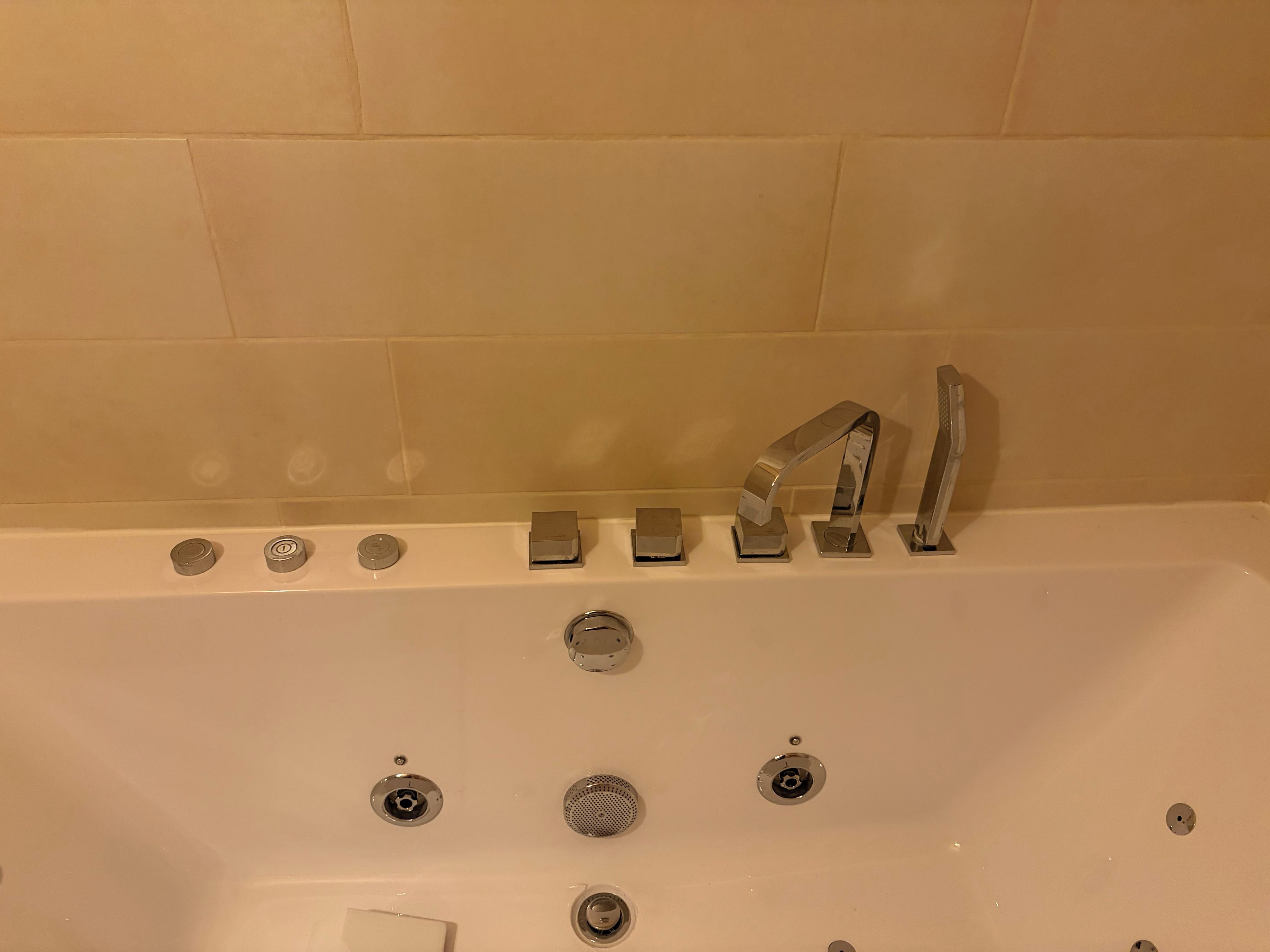 A bathtub with multiple faucets and a drain.