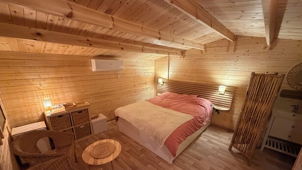 Ein Schlafzimmer einer Holzhütte mit einem Bett, Nachttischen, einem Sessel und einem kleinen Tisch.