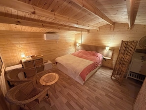 A wooden cabin bedroom with a bed, bedside tables, a chair, and a small table.