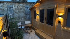 Eine Holzhütte mit Kiesterrasse, einem Holztisch und Stühlen sowie einer Steinmauer.
