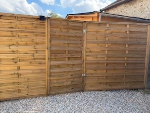 A wooden fence with a gate, gravel ground, and a building in the background.