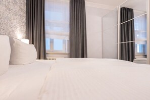 Ein Hotelzimmer mit einem großen Bett, einem Fenster mit Vorhängen, einem Heizkörper und einer Wand mit einer strukturierten Oberfläche.