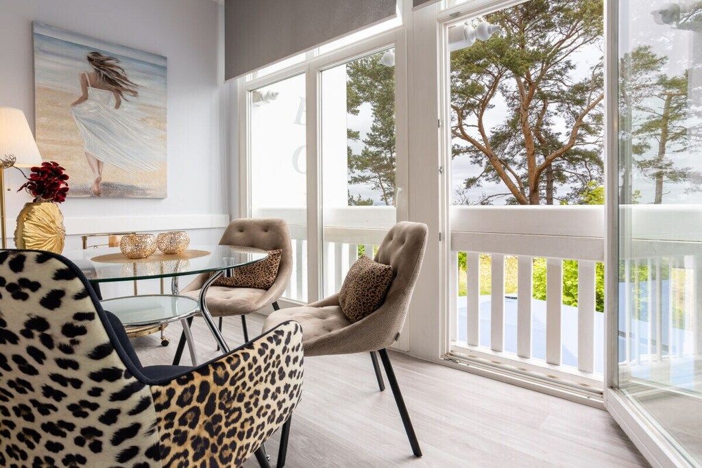 A dining area with a glass table, two chairs with leopard print upholstery, and a painting of a woman on the wall.