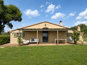 Einbungalow mit überdachter Veranda, Eingangstür und einer kleinen Terrasse mit Gartenmöbeln.
