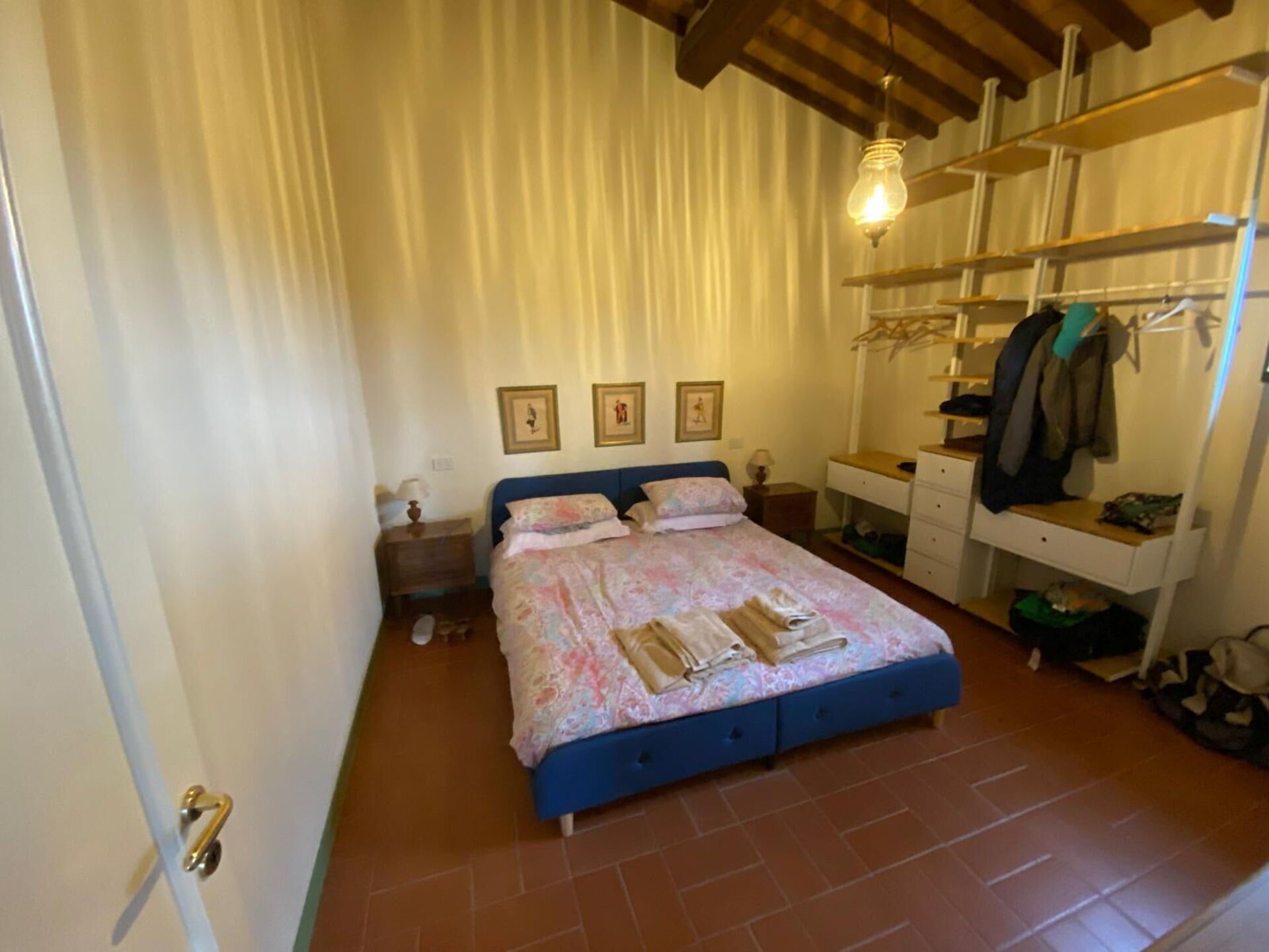 A bedroom with a bed, a bedside table, a wardrobe, and a hanging light fixture.