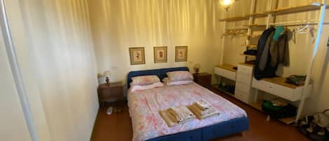 A bedroom with a bed, a bedside table, a wardrobe, and a hanging light fixture.
