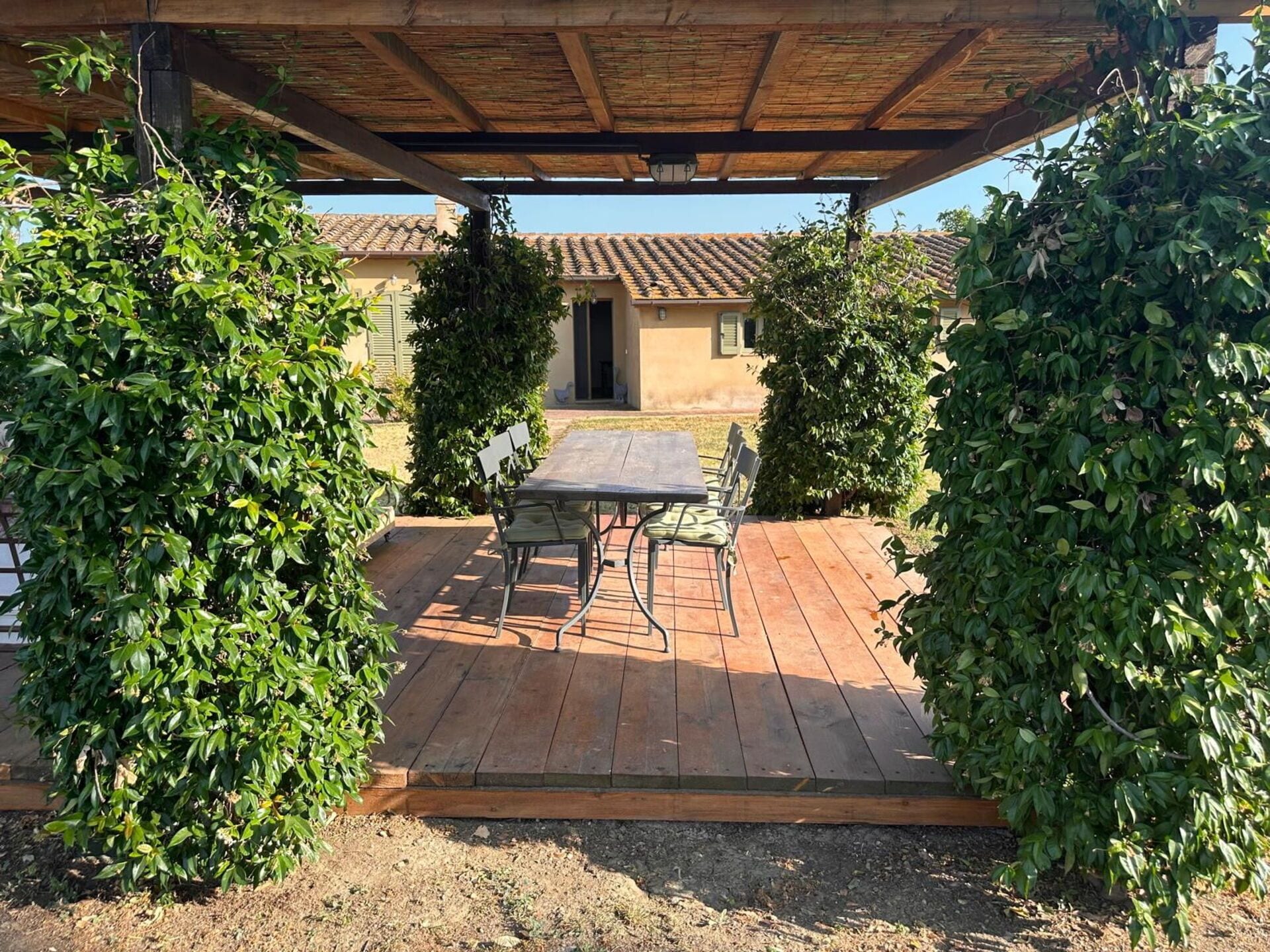 A covered patio area with a table and chairs, surrounded by greenery.